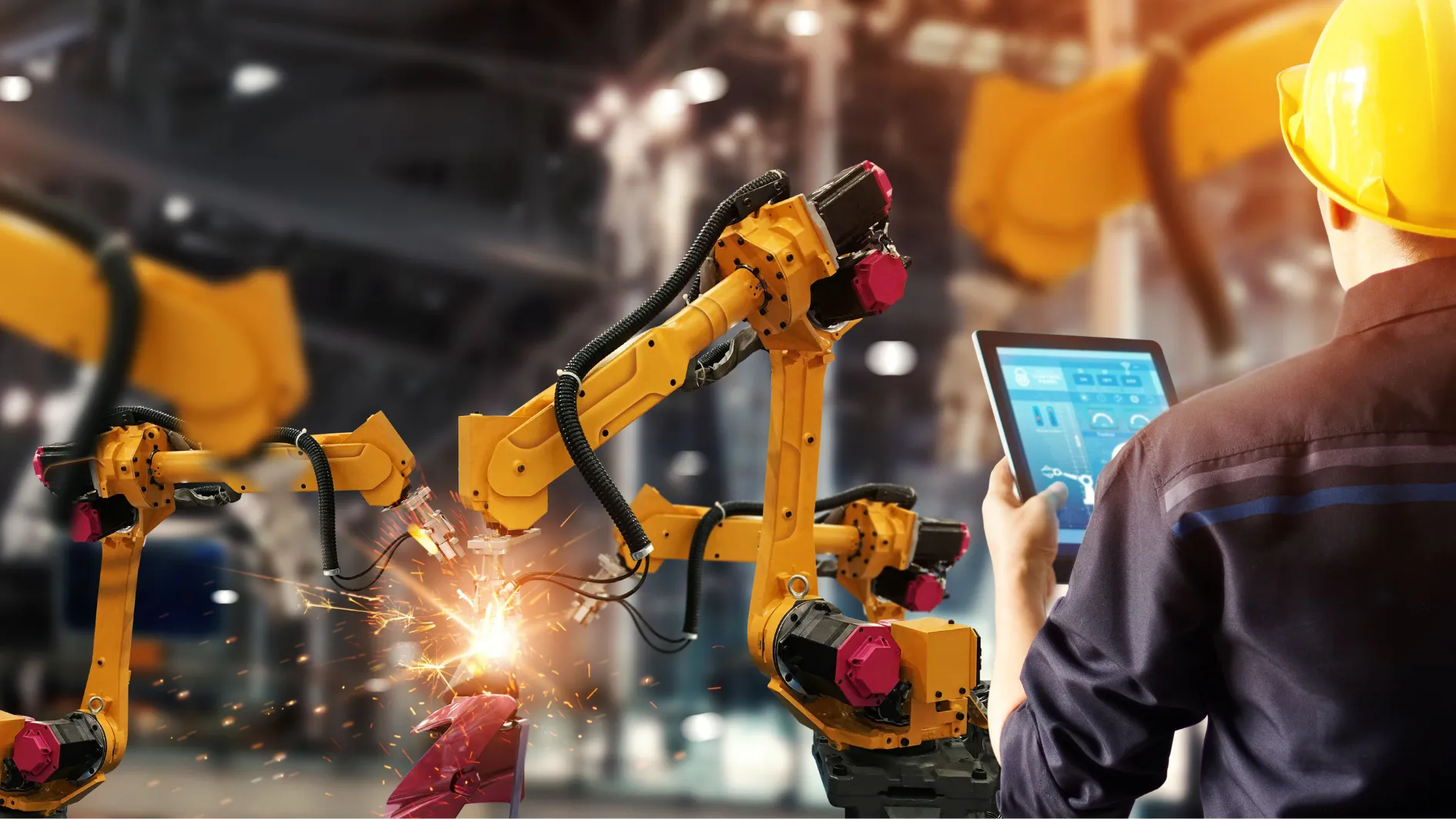 Engineer with a tablet monitoring robotic arms on a production line